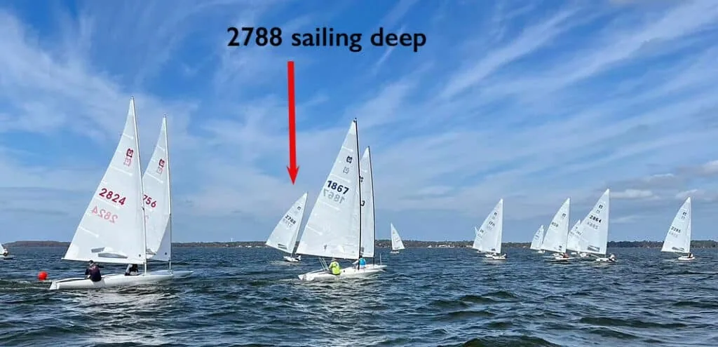 Fleet of dinghies racing downwind, one boat marked as sailing deep