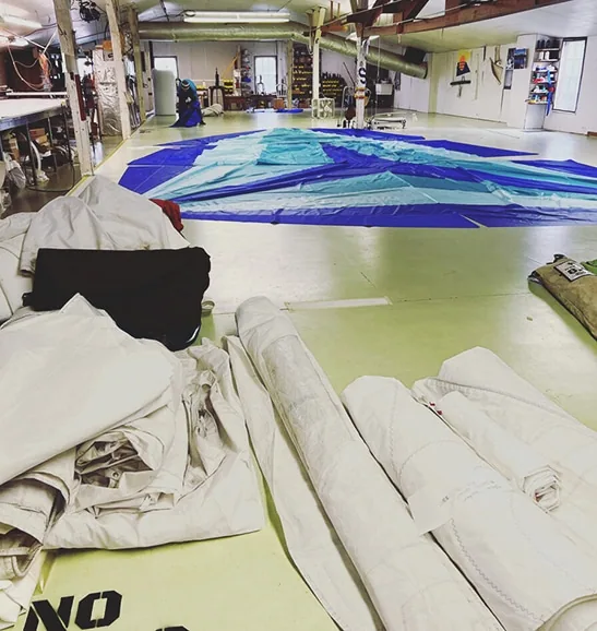 ScandiaSails loft floor with a blue spinnaker laid out and sails rolled nearby