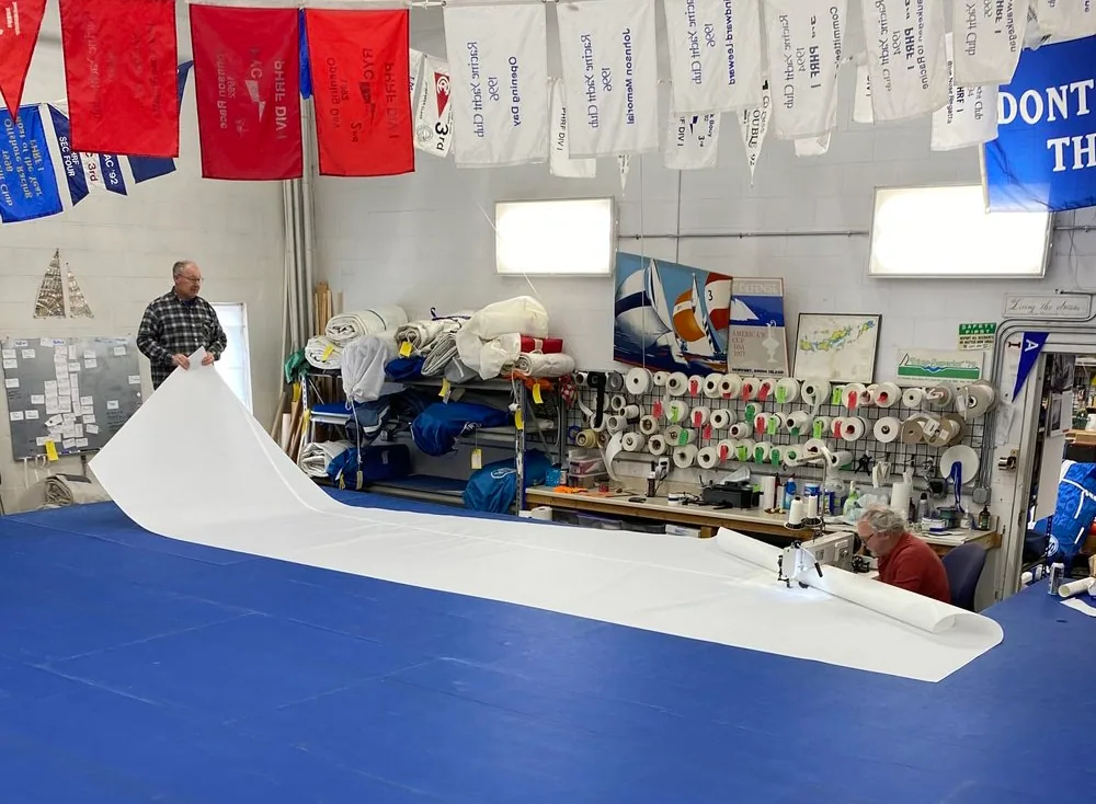 Sailmaker feeding a large white sail panel through a loft sewing machine