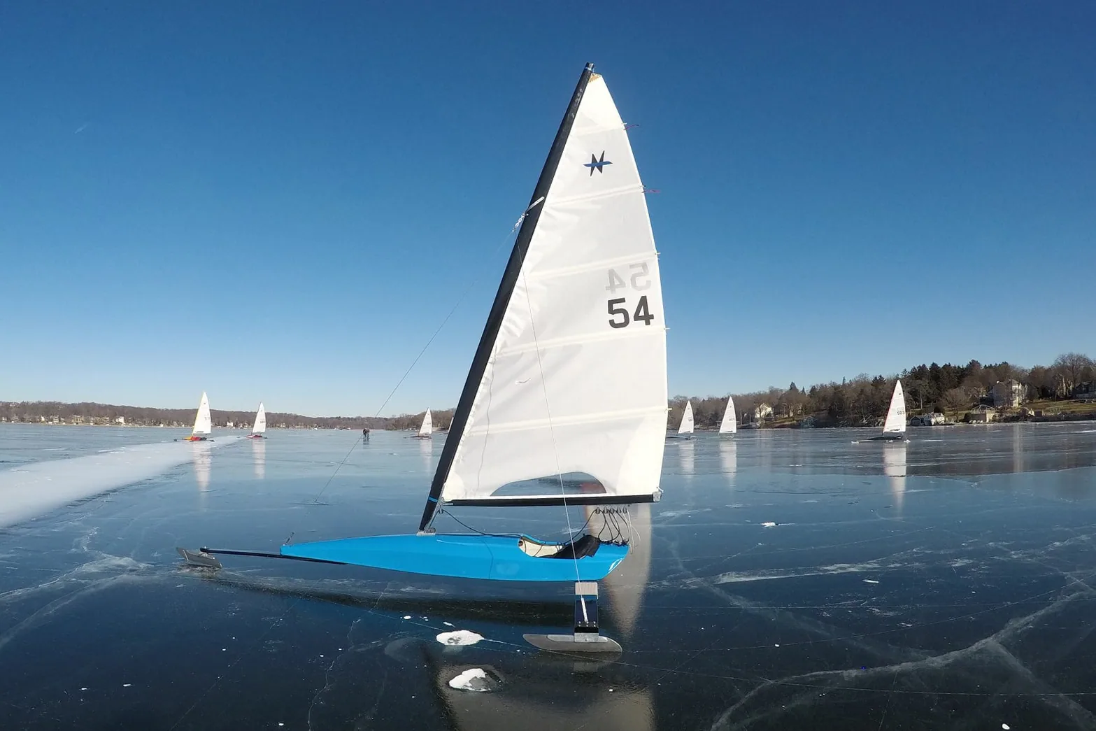 DN ice boat under sail on a frozen lake, other iceboats visible in the distance