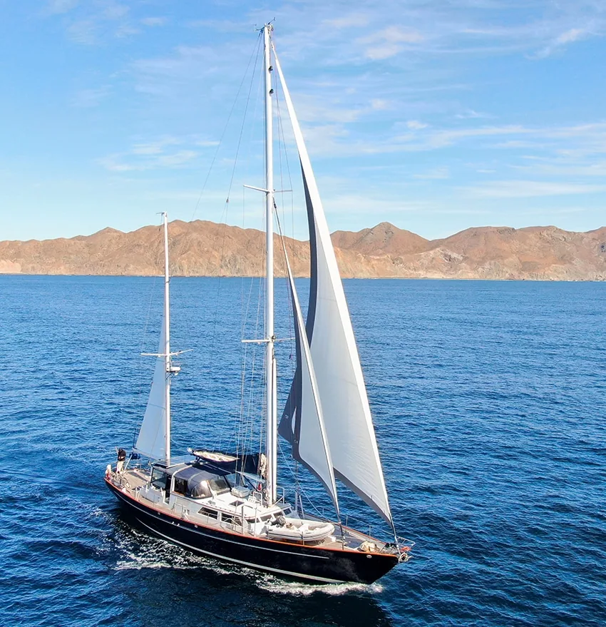 Black-hulled cruising yacht under sail off Mexico's desert coastline