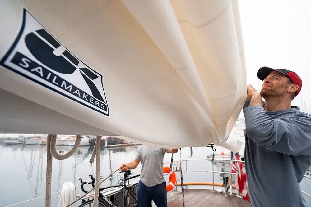 UK Sailmakers loft crew inspecting a sail with the diamond logo at the dock