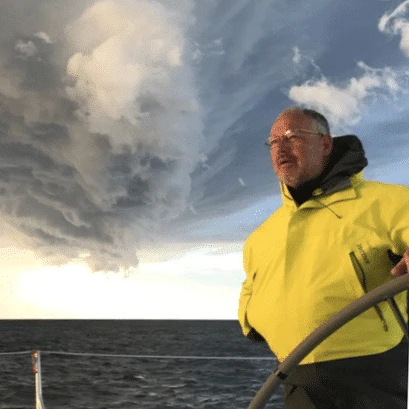 Portrait of a man in yellow foul-weather gear at the helm with storm clouds behind