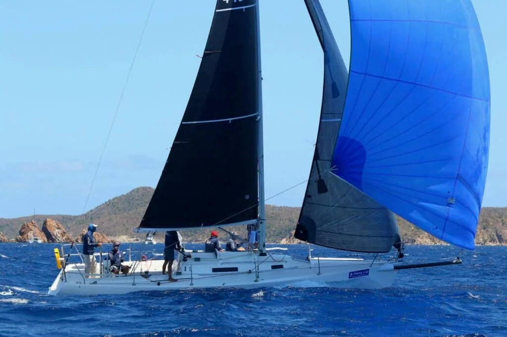 J/105 Jenk flying a blue spinnaker downwind past a rocky BVI headland