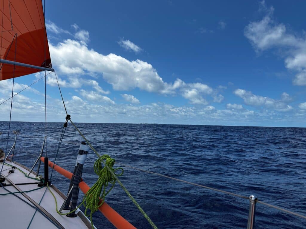 Bow view offshore under an orange sail during Leg 1 of the Bermuda 1-2