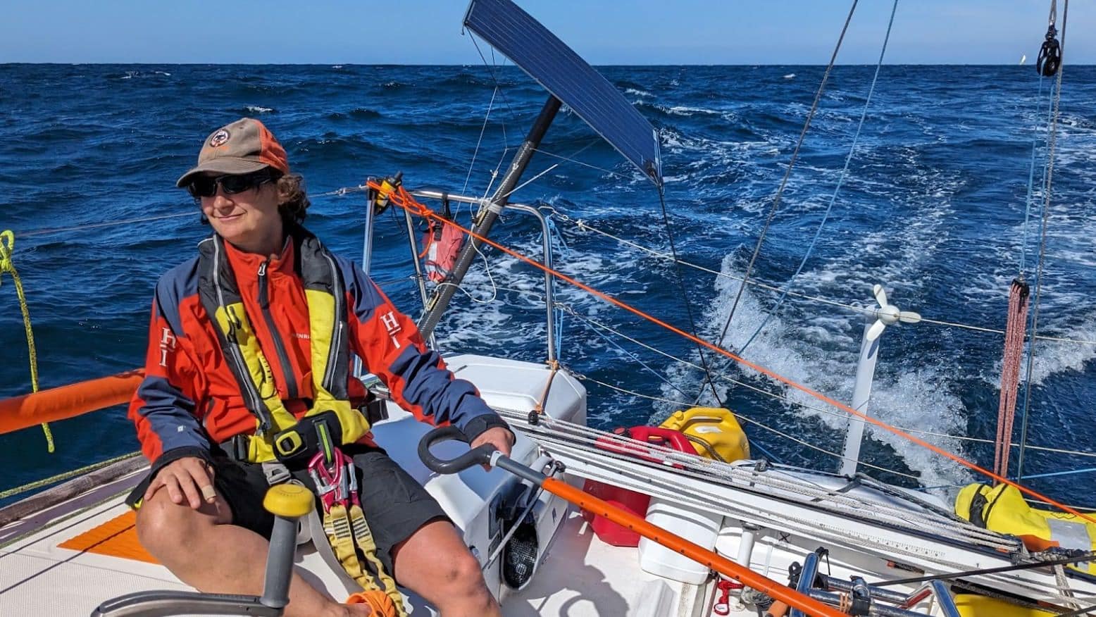 Sailor at the helm of Figaro 2 ENVOLEÉ, steering downwind in bright conditions