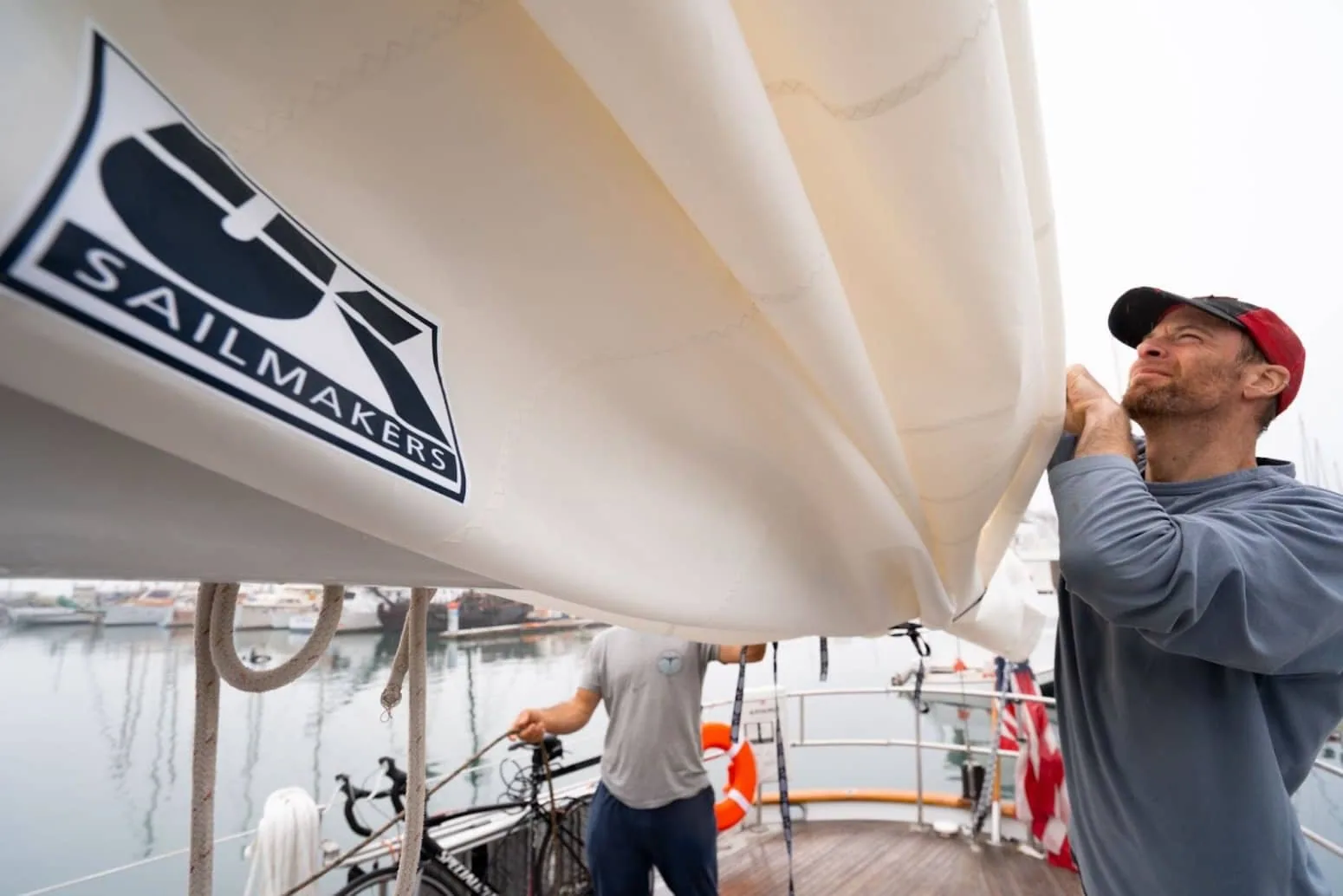 Crew member fitting a UK Sailmakers branded sail cover on deck