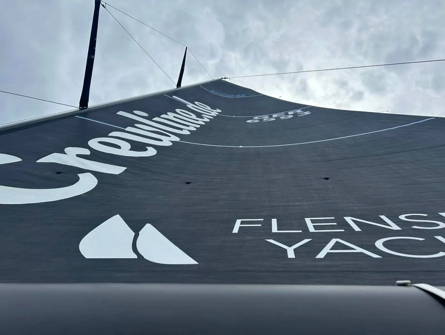 Close-up of KATIMA's dark mainsail with Crewline.de and Flensburger Yacht Club branding