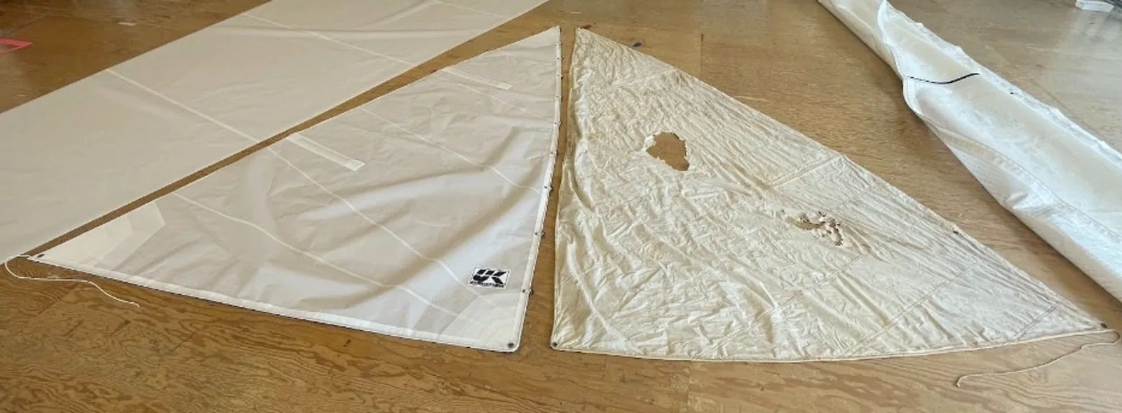 Sail panels laid out on the loft floor, one showing a repaired tear