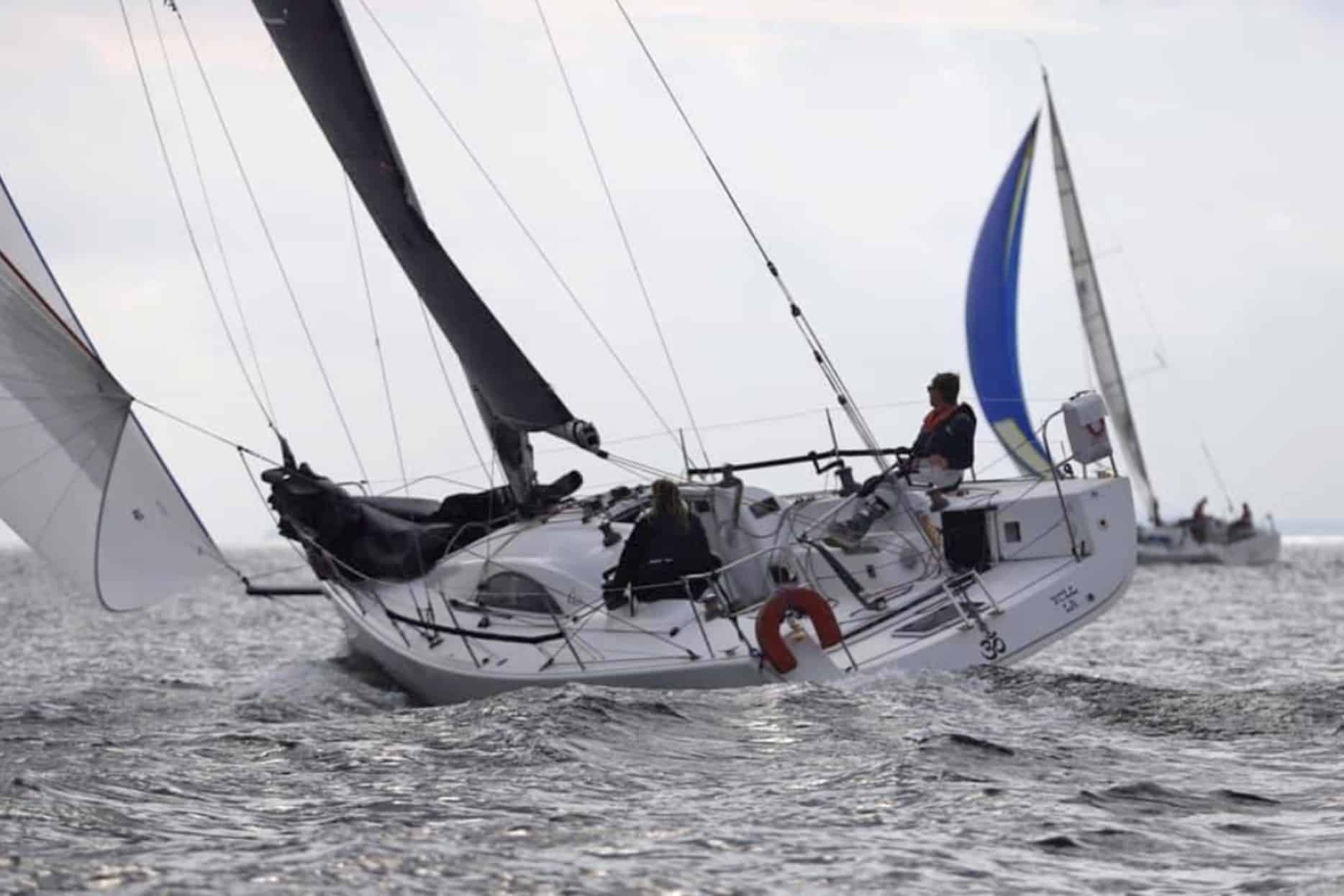 Shorthanded racing yacht reaching hard with a spinnaker flying in the background