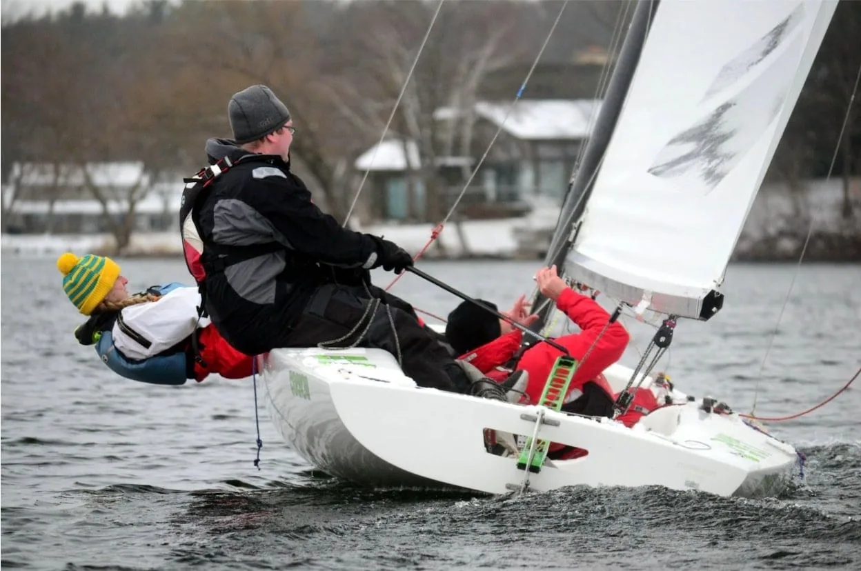 Sailor hiking hard on a one-design dinghy during cold-weather racing on a lake