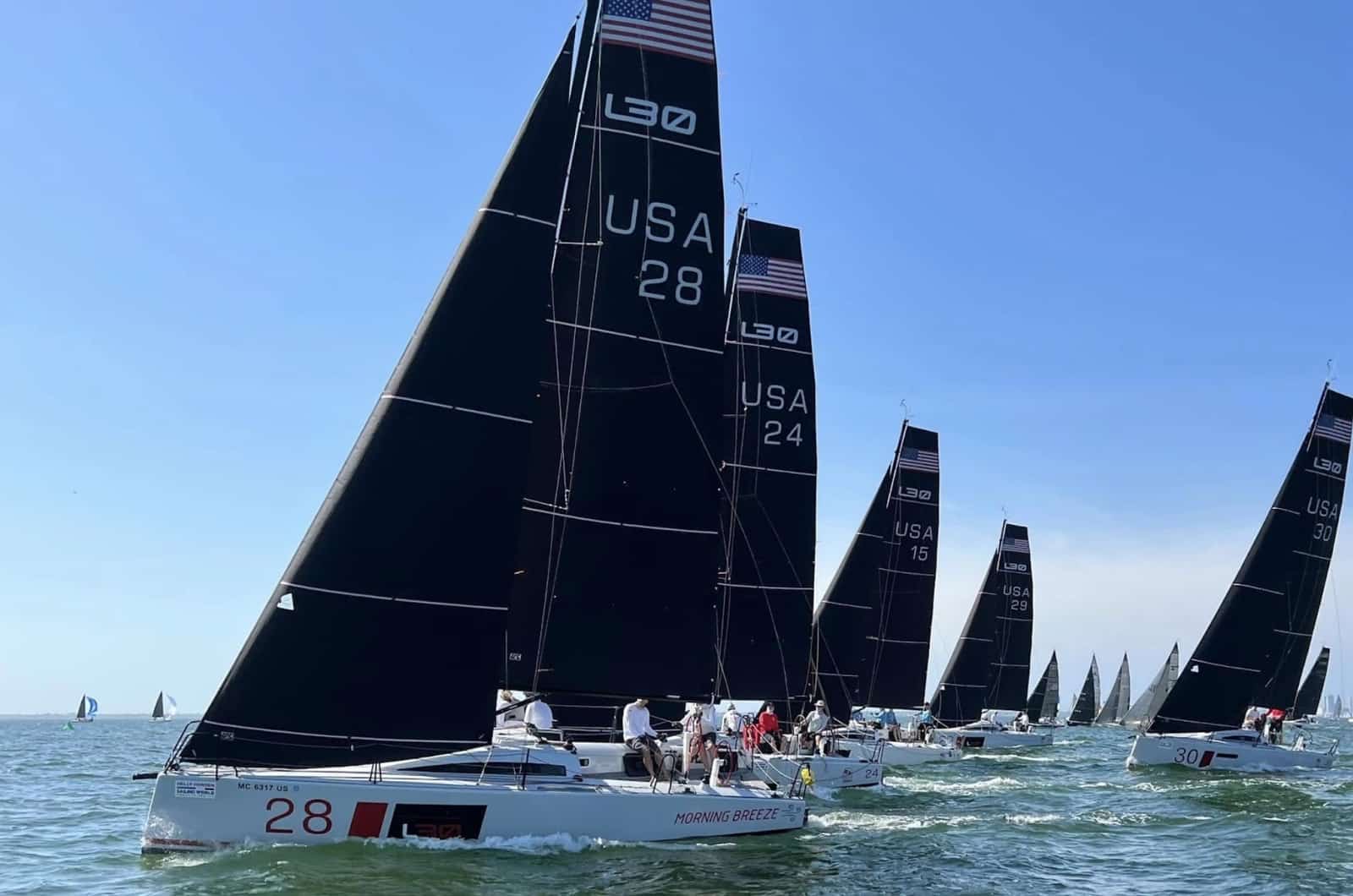 Fleet of L30 one-design yachts racing upwind under black sails