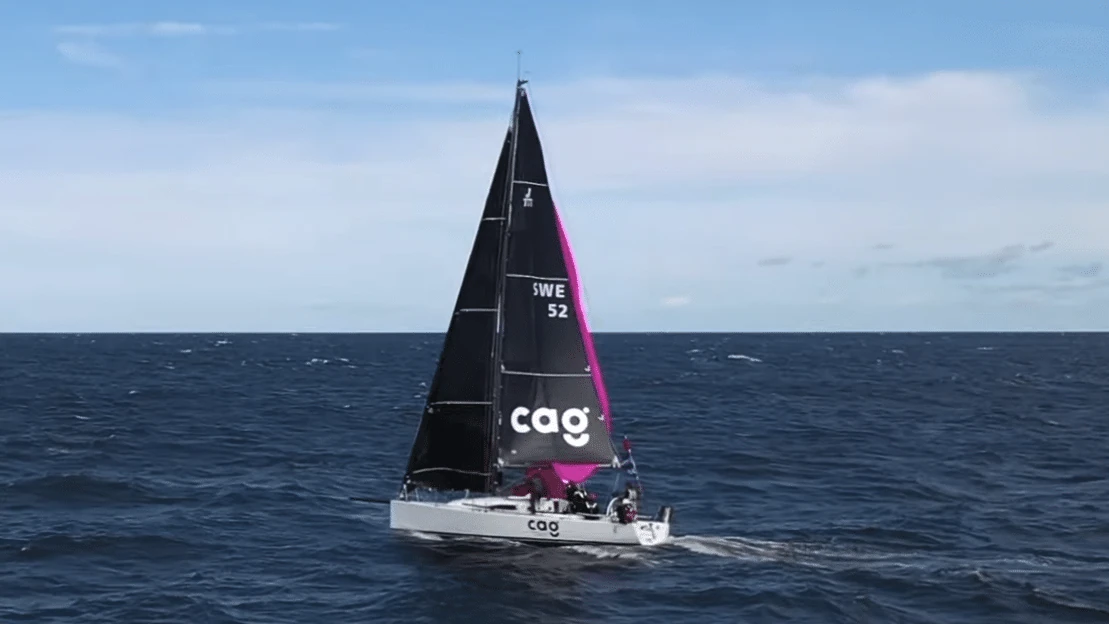 Sailboat CAG heeled under a black and pink mainsail on open water