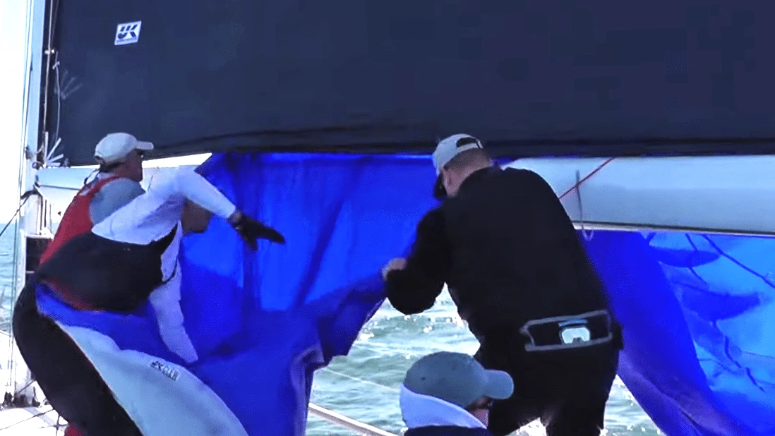 Crew stuffing a blue spinnaker down the companionway during a letterbox douse