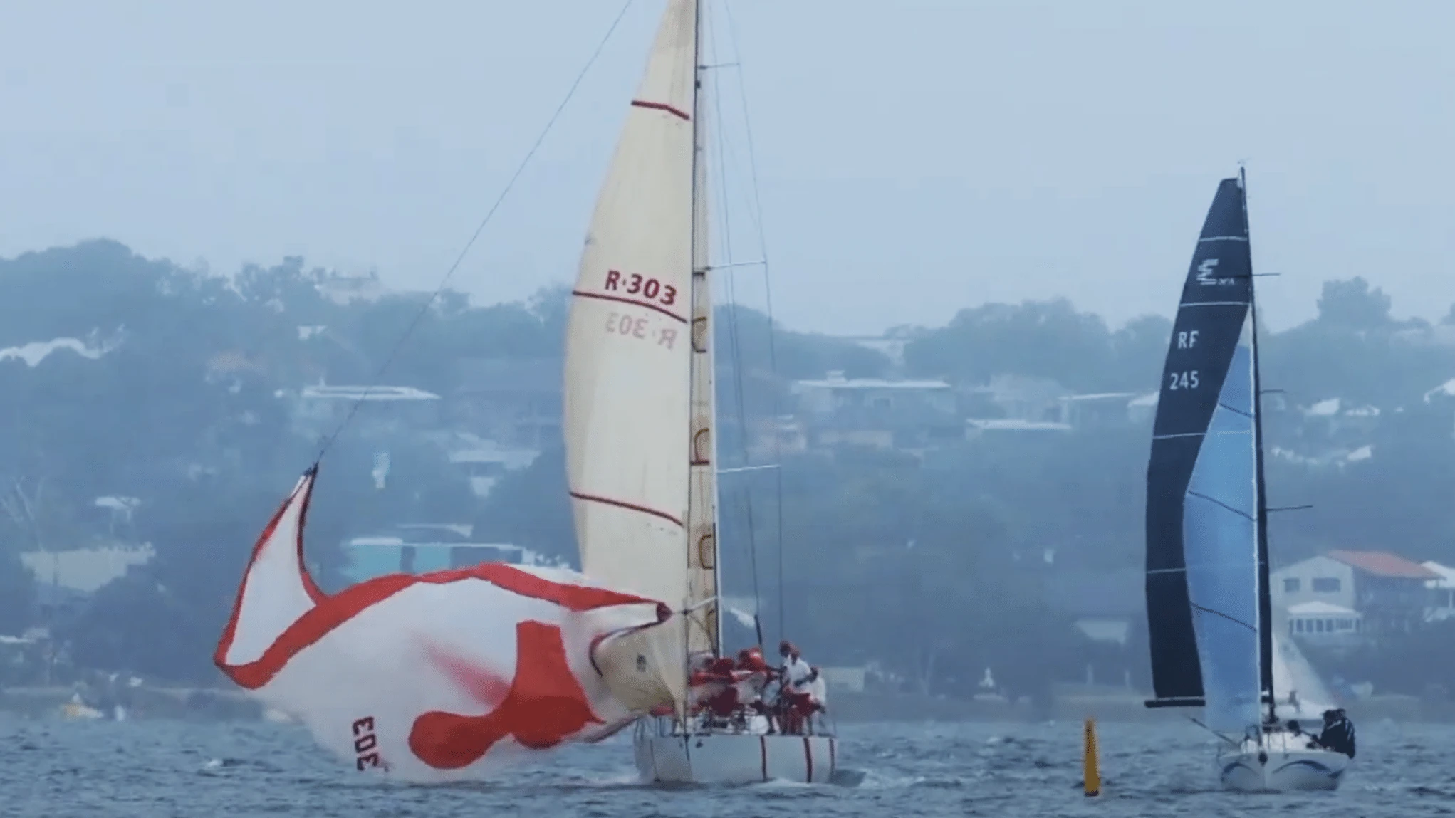 Boat R-303 dousing a red and white spinnaker alongside another yacht racing nearby
