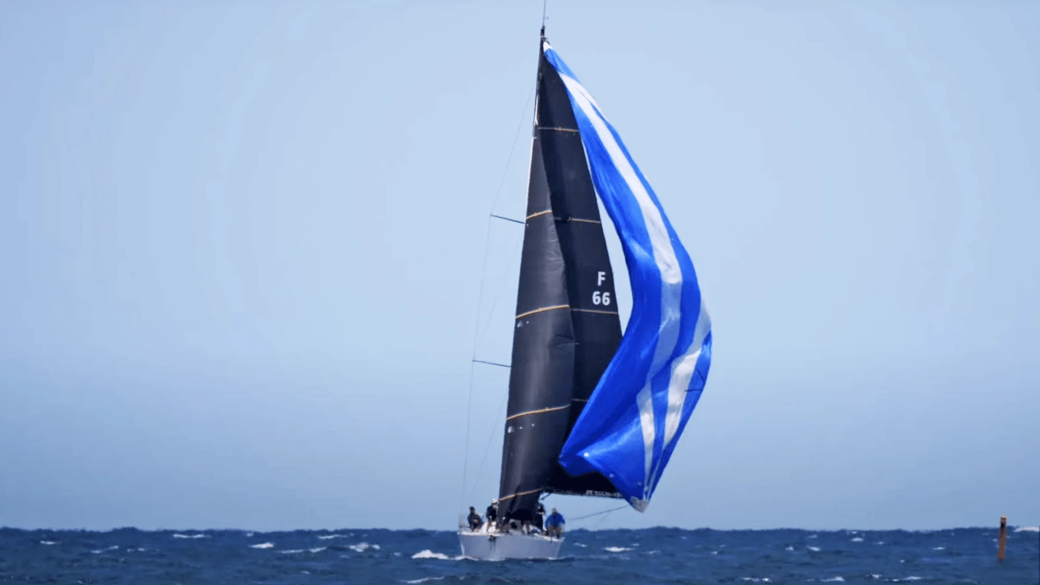 Sailboat F66 running downwind under a black mainsail and blue and white spinnaker