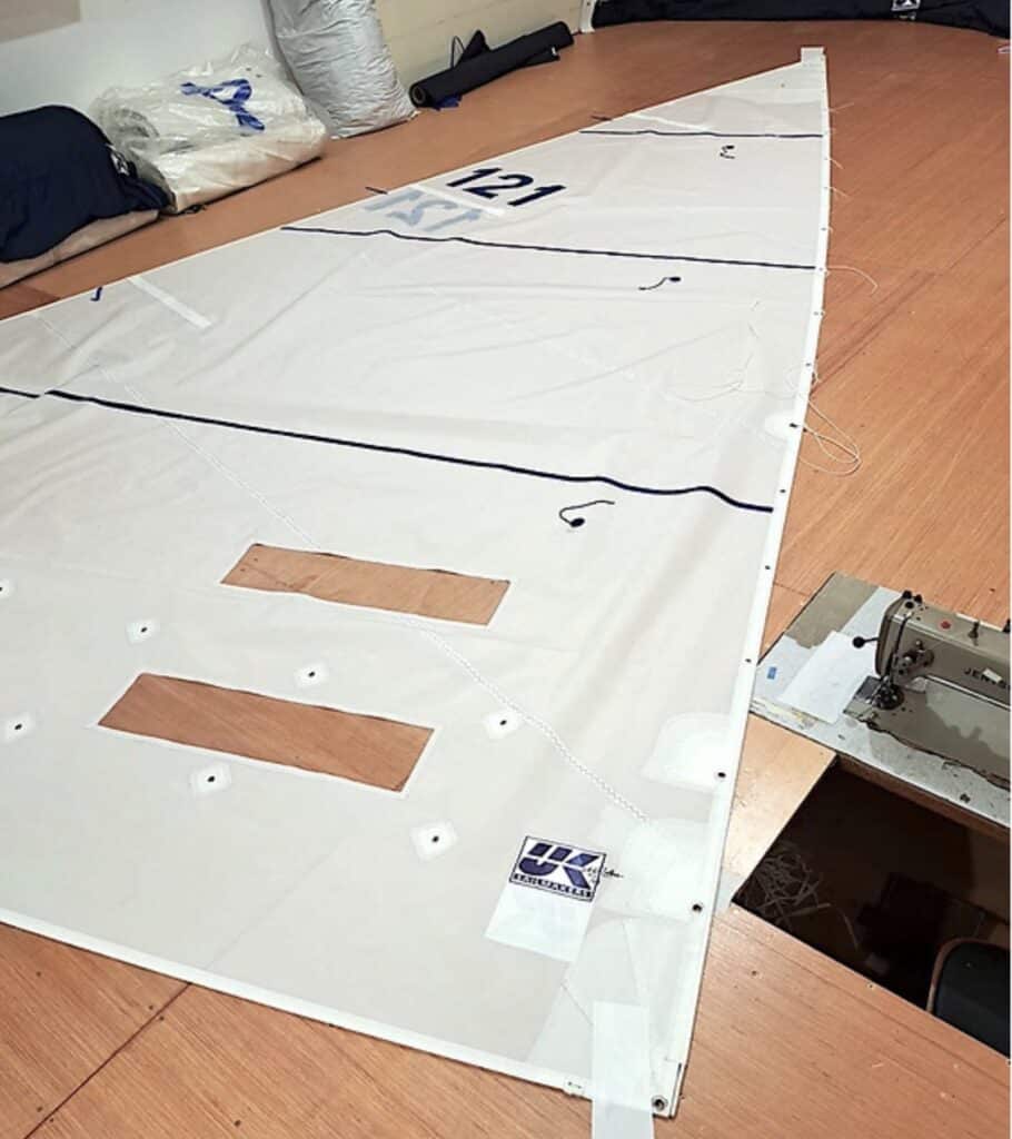 New sail numbered 121 laid flat on the loft floor beside a sewing machine
