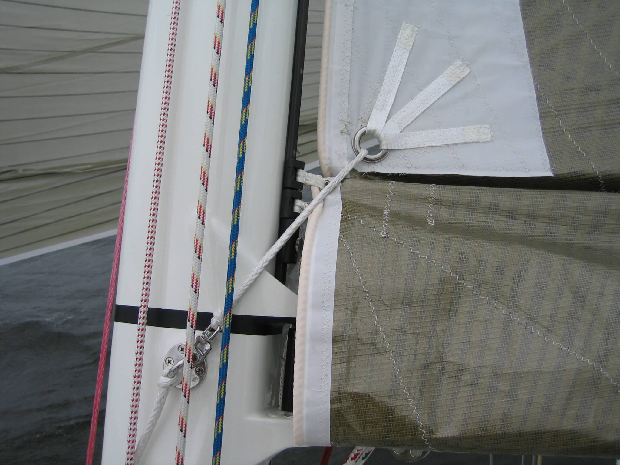 Reef tack grommet lashed with white Dyneema line at the mast, beside the halyard cars