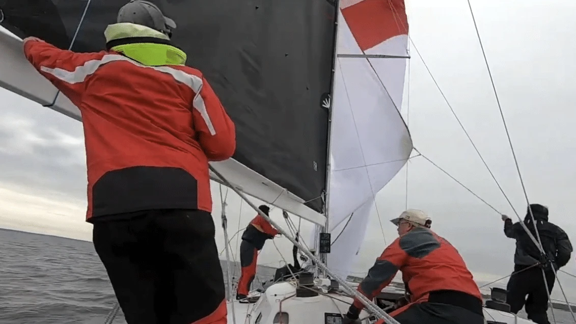 Crew bracing on the rail as the mainsail and spinnaker flog during a late gybe