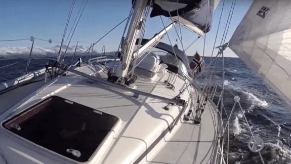 Sailing on deck past snow-capped mountains, mainsail leech visible overhead