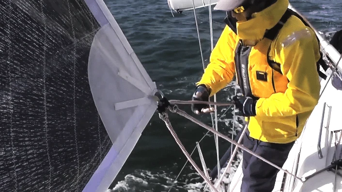 Crew in a yellow jacket trimming a genoa led to an outboard block near the rail