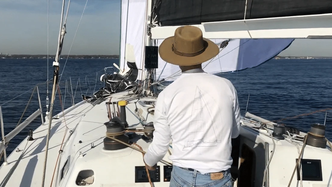 Sailor in a straw hat single-handing the helm and looking forward