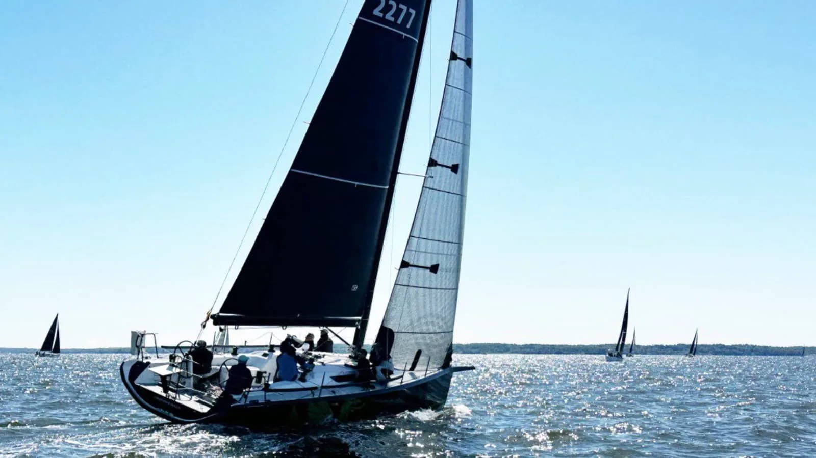 Racing yacht sail number 2277 heeled under dark sails with a boat in the distance