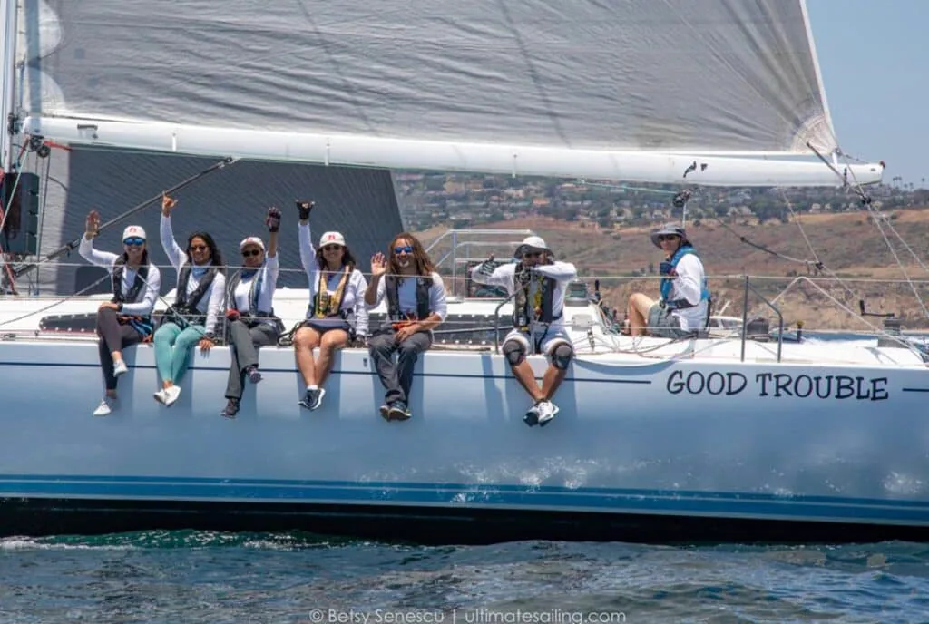 GOOD TROUBLE crew hiking out and cheering as the boat reaches under sail
