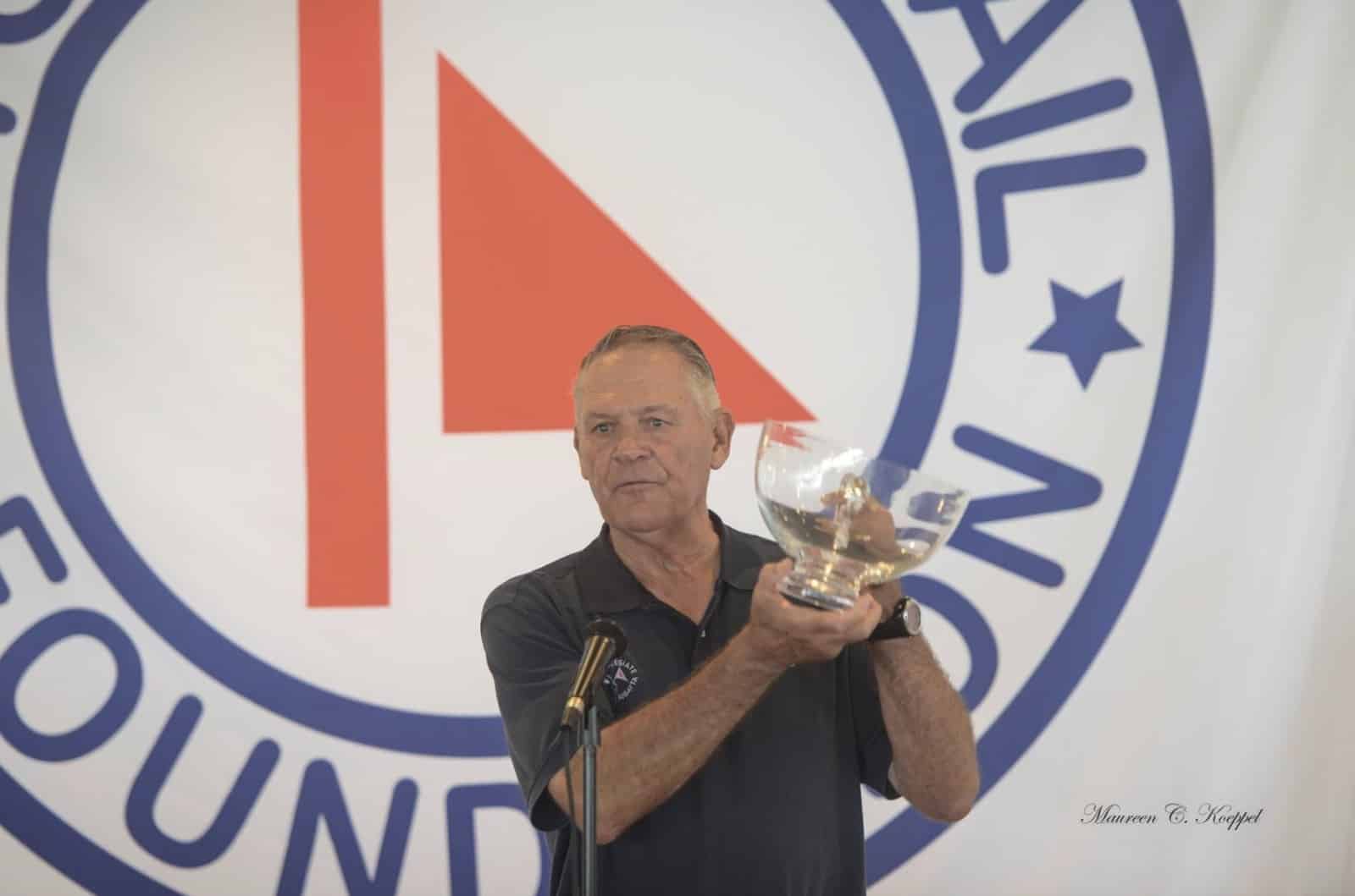 Butch Ulmer presenting a glass trophy at a podium in front of a sailing foundation backdrop
