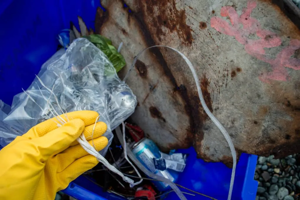 Gloved hand pulling plastic debris from a beach cleanup bin