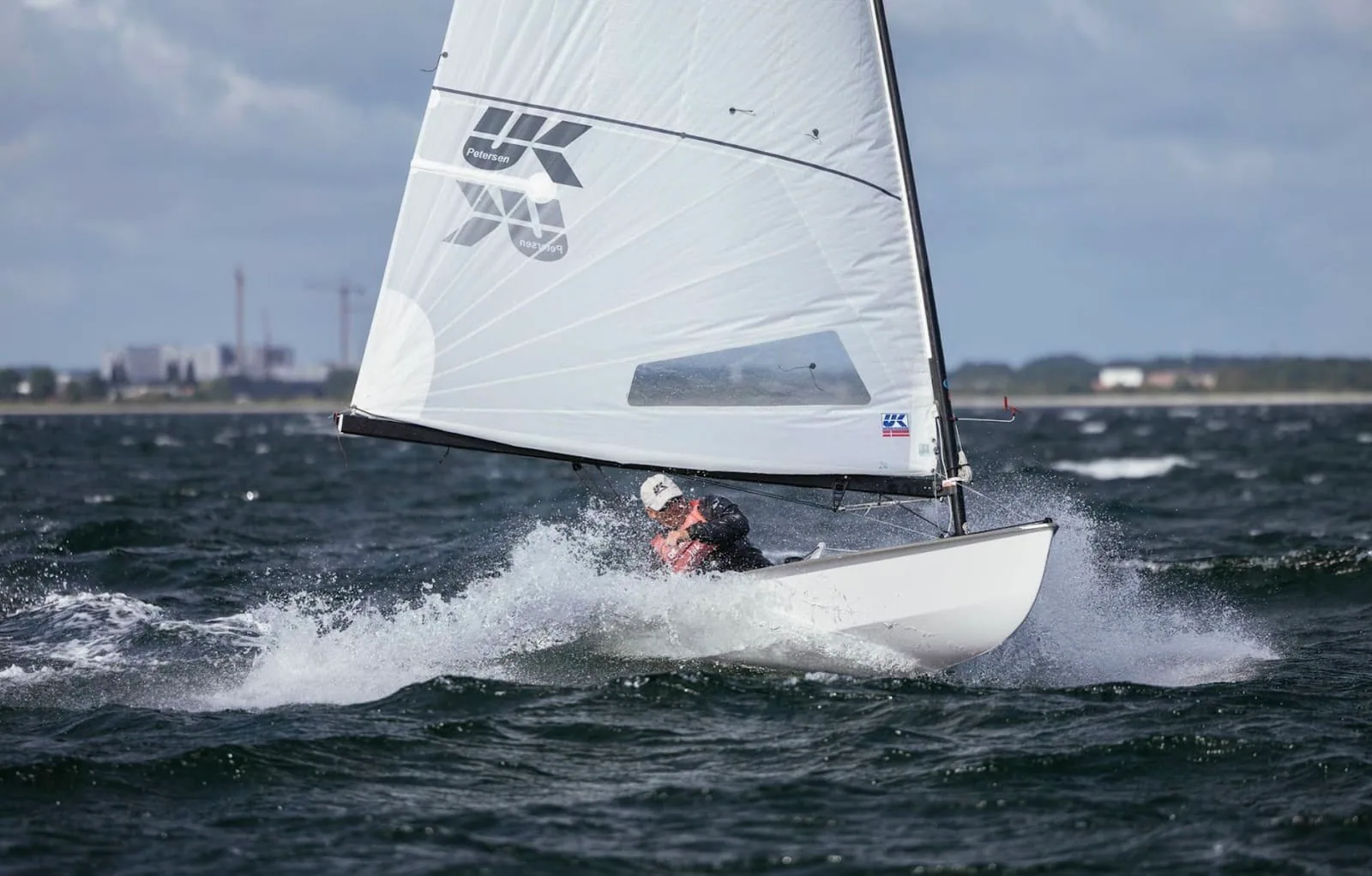 OK Dinghy sailor heeled hard with spray flying, X-Drive® sail visible