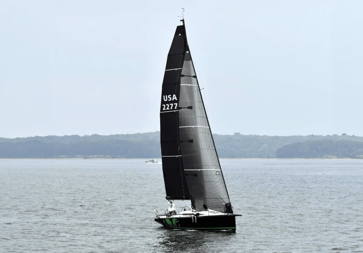 Black-sailed sloop USA 2277 sailing calm water near a tree-lined shore