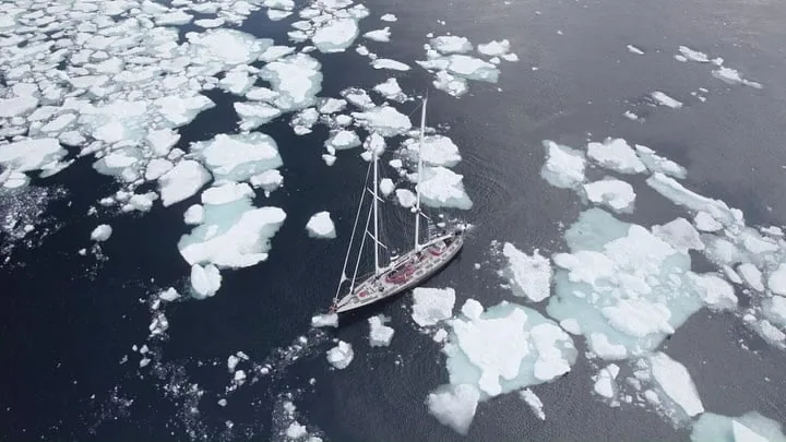 Two-masted sailboat threading through broken sea ice, aerial view