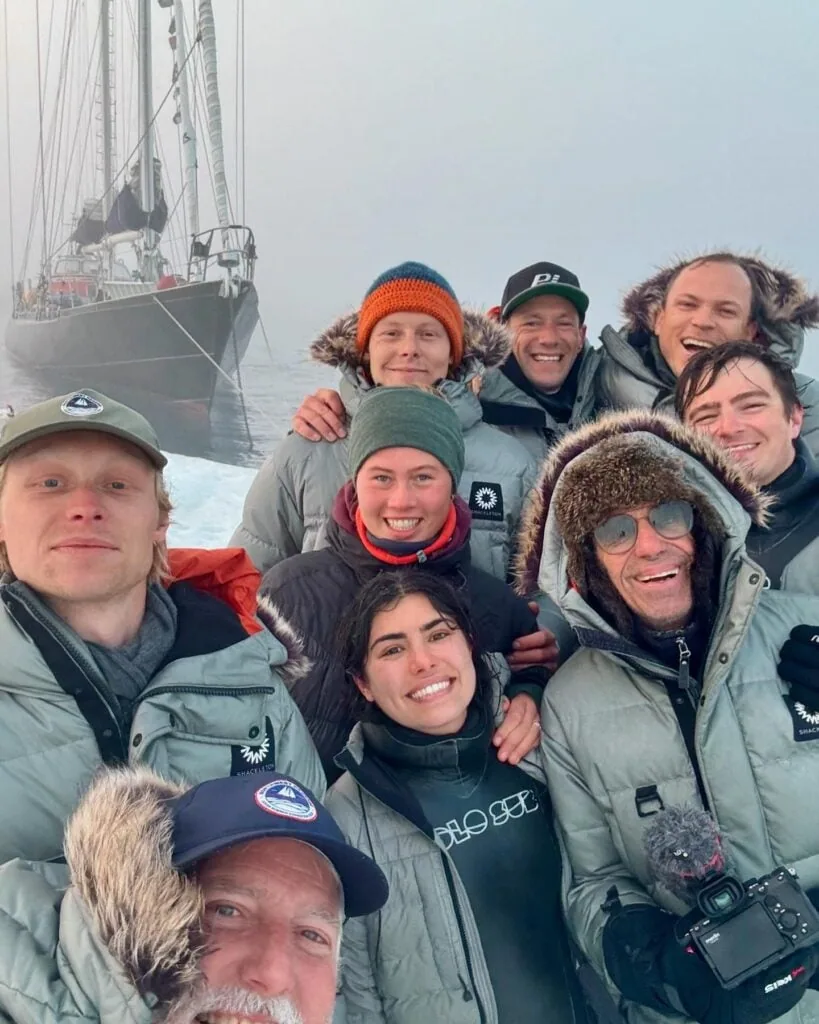 Ocean Science Expedition crew bundled in parkas gather for a group photo with ABEL TASMAN's rig in fog behind them.
