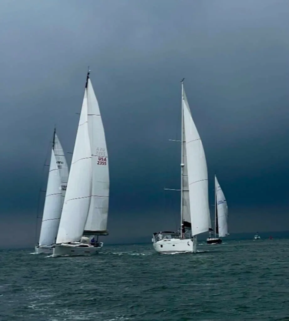 Two sailboats, one flying sail number USA 2395, race under a darkening storm sky.