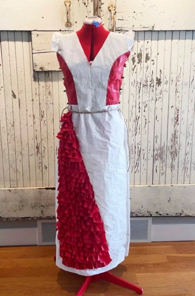 Half-finished red-and-white sailcloth gown with ruffled trim, displayed on a dress form.