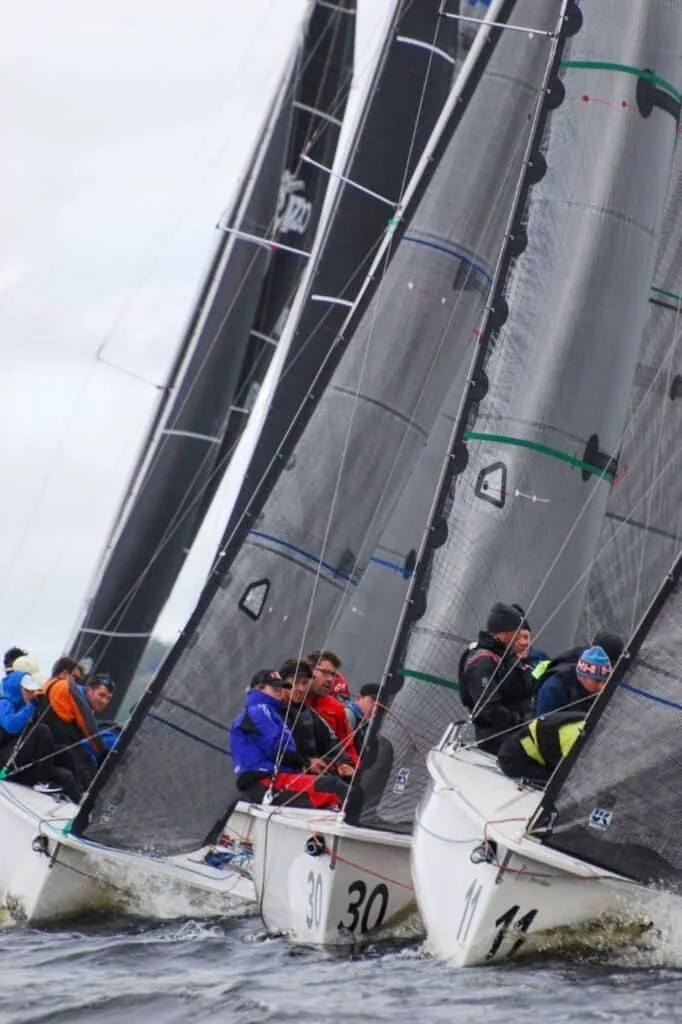 Three 1720 Sportsboats, numbered 30 and 11, sail close together under black sails.