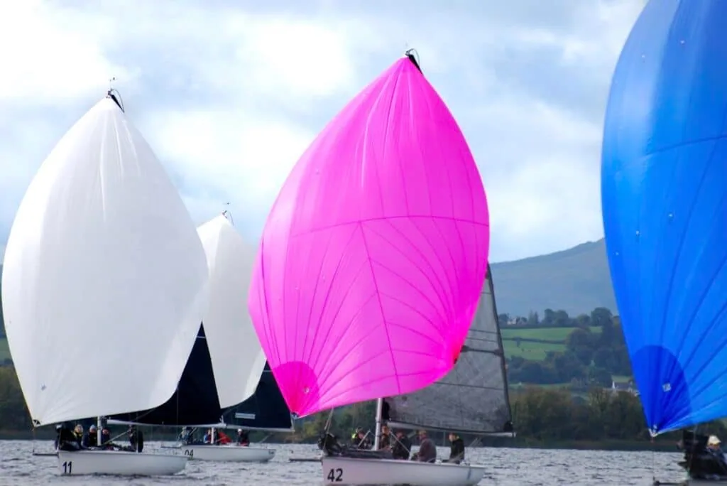 1720 Sportsboats numbered 11 and 42 race under white and pink spinnakers, blue one nearby.