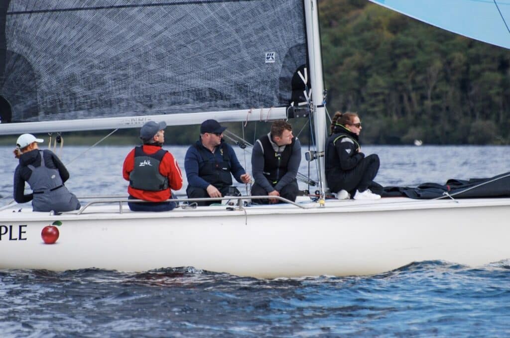 Five crew sit along the rail of a 1720 Sportsboat under a dark asymmetric spinnaker.