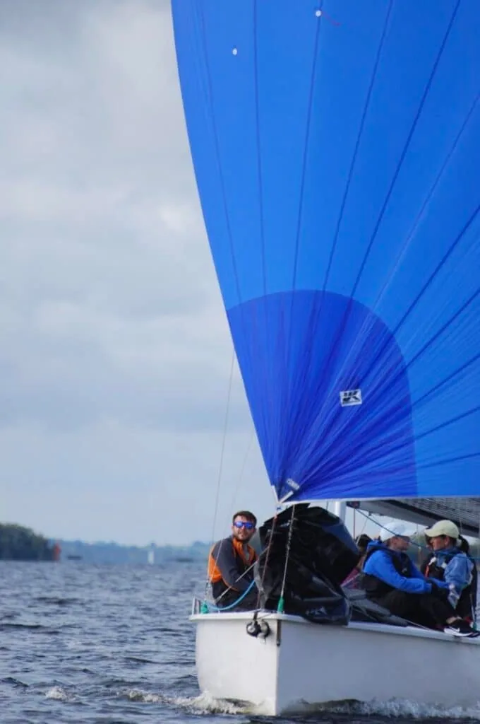 Three crew sail a 1720 Sportsboat downwind under a full blue spinnaker.