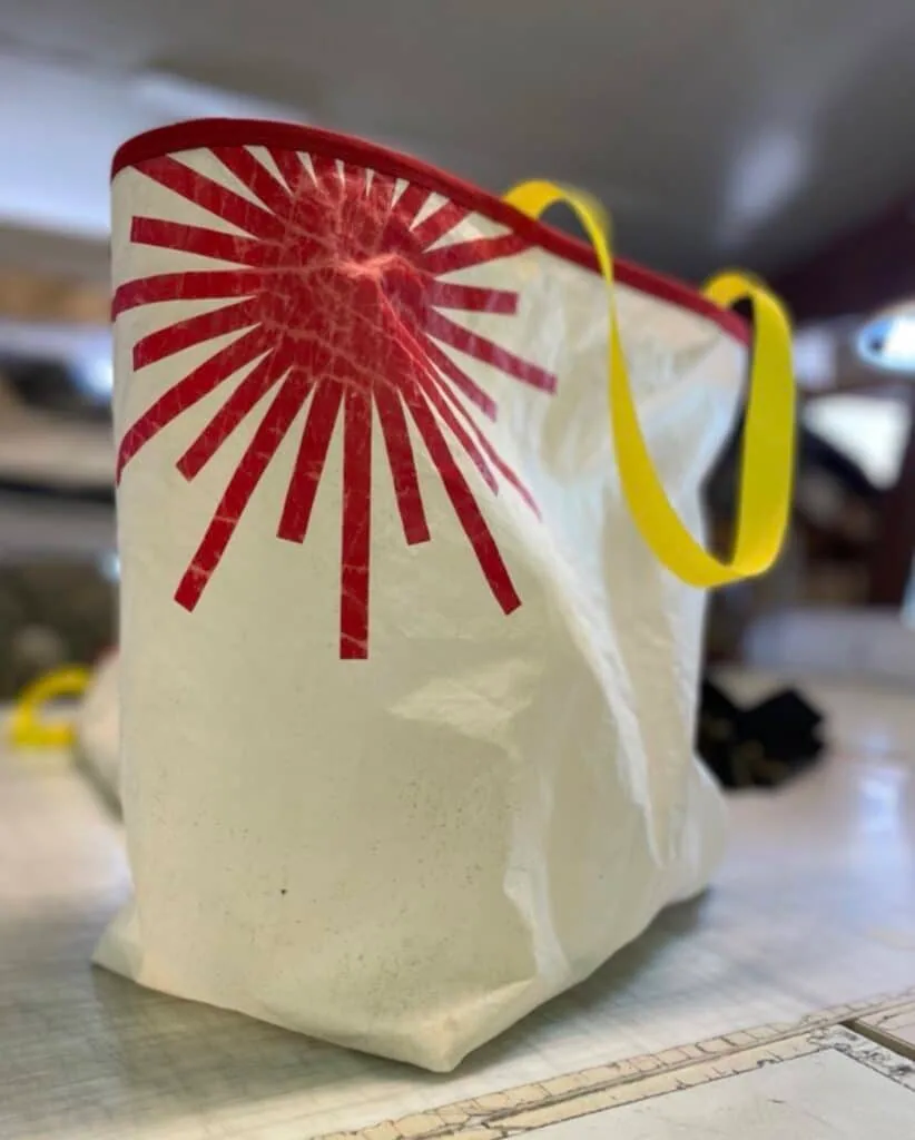 Cream sailcloth tote bag with a red sunburst appliqué and yellow woven handles.