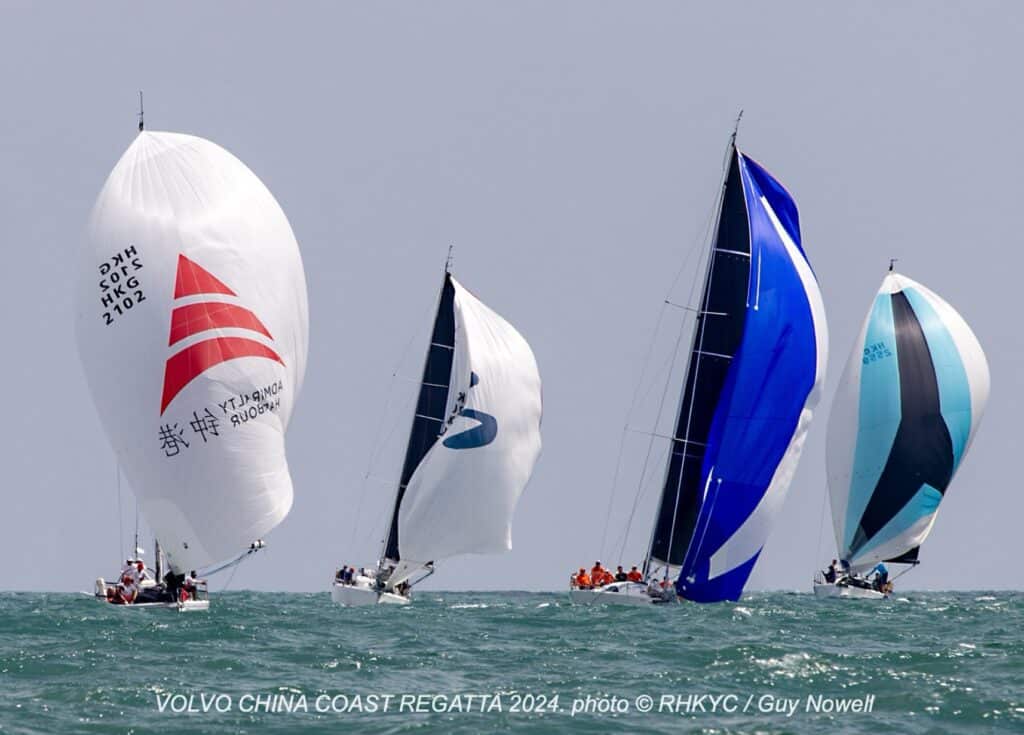 Four yachts race downwind under red, white, and blue spinnakers at the China Coast Regatta.