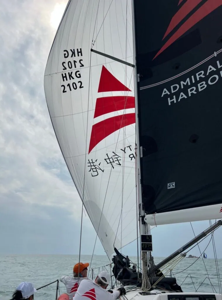 Close-up of HKG 2102's red compass-rose spinnaker beside a dark Admiral Harbour mainsail.