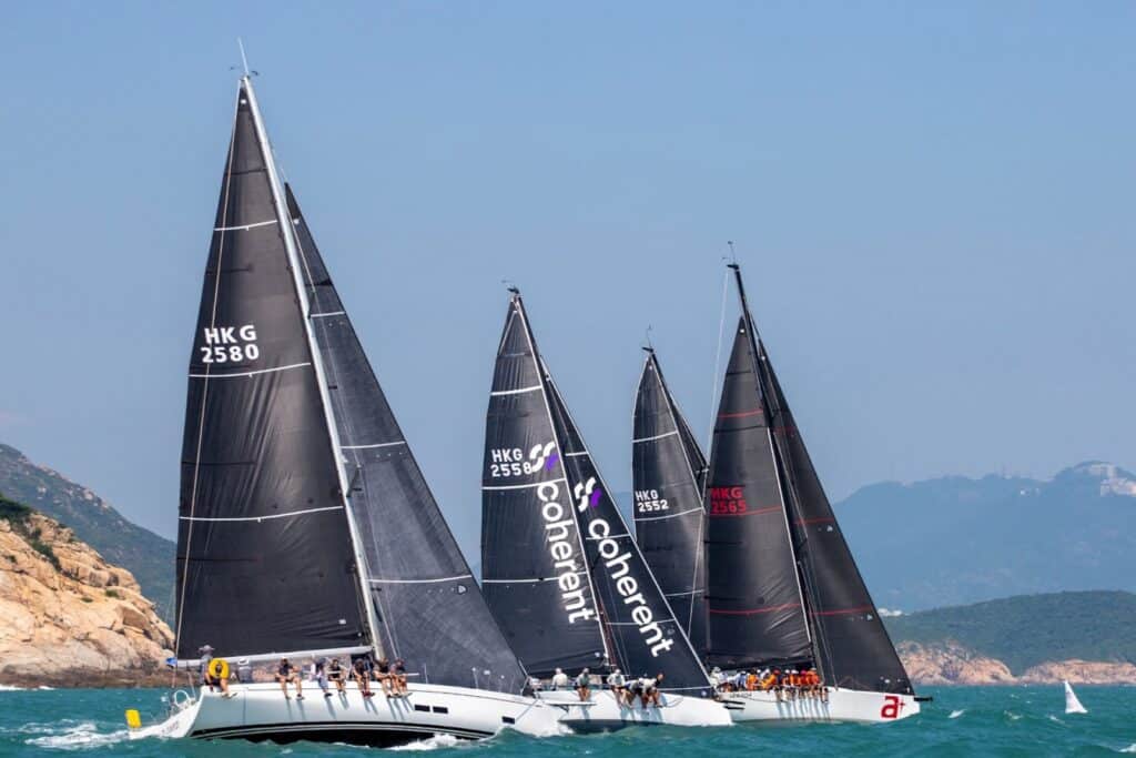 Three yachts race upwind under black sails, two branded with the Coherent sponsor logo.