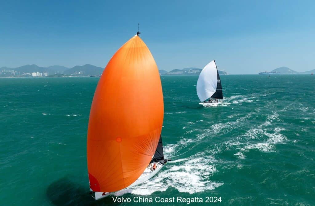 Aerial view of two yachts racing downwind, one under a bright orange spinnaker.