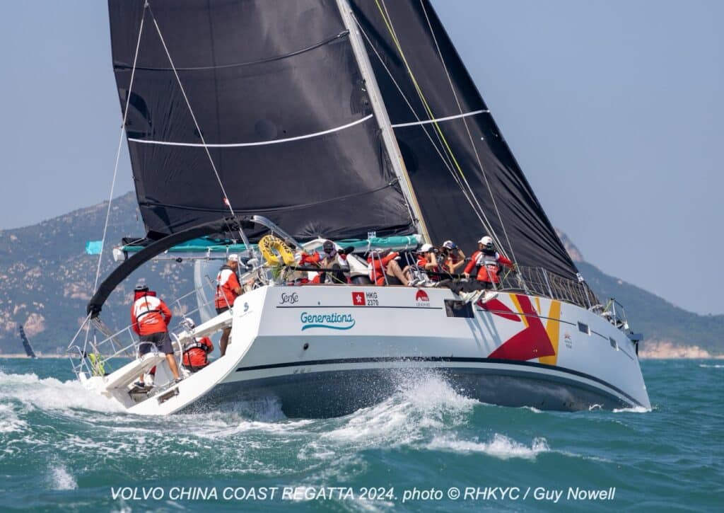 GENERATIONS heels hard with crew in orange life jackets under a black spinnaker.