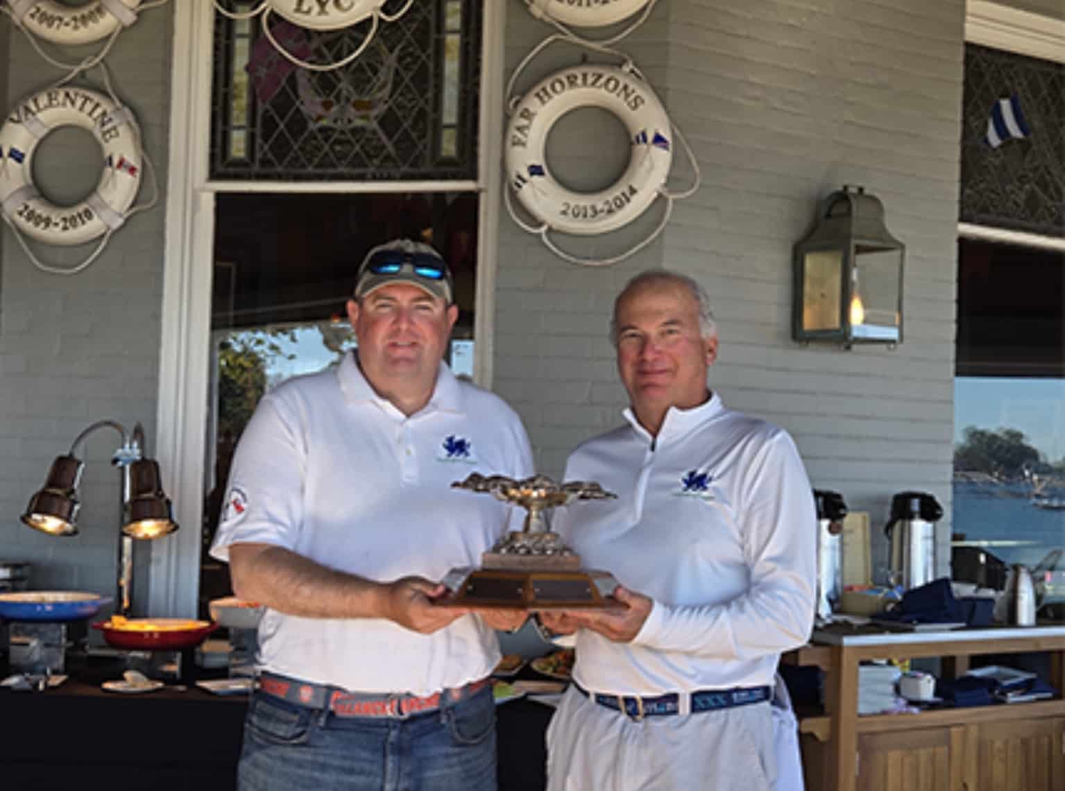 Colin Fitzpatrick and Andrew Weiss hold their Bitter Ender trophy on a yacht club porch.