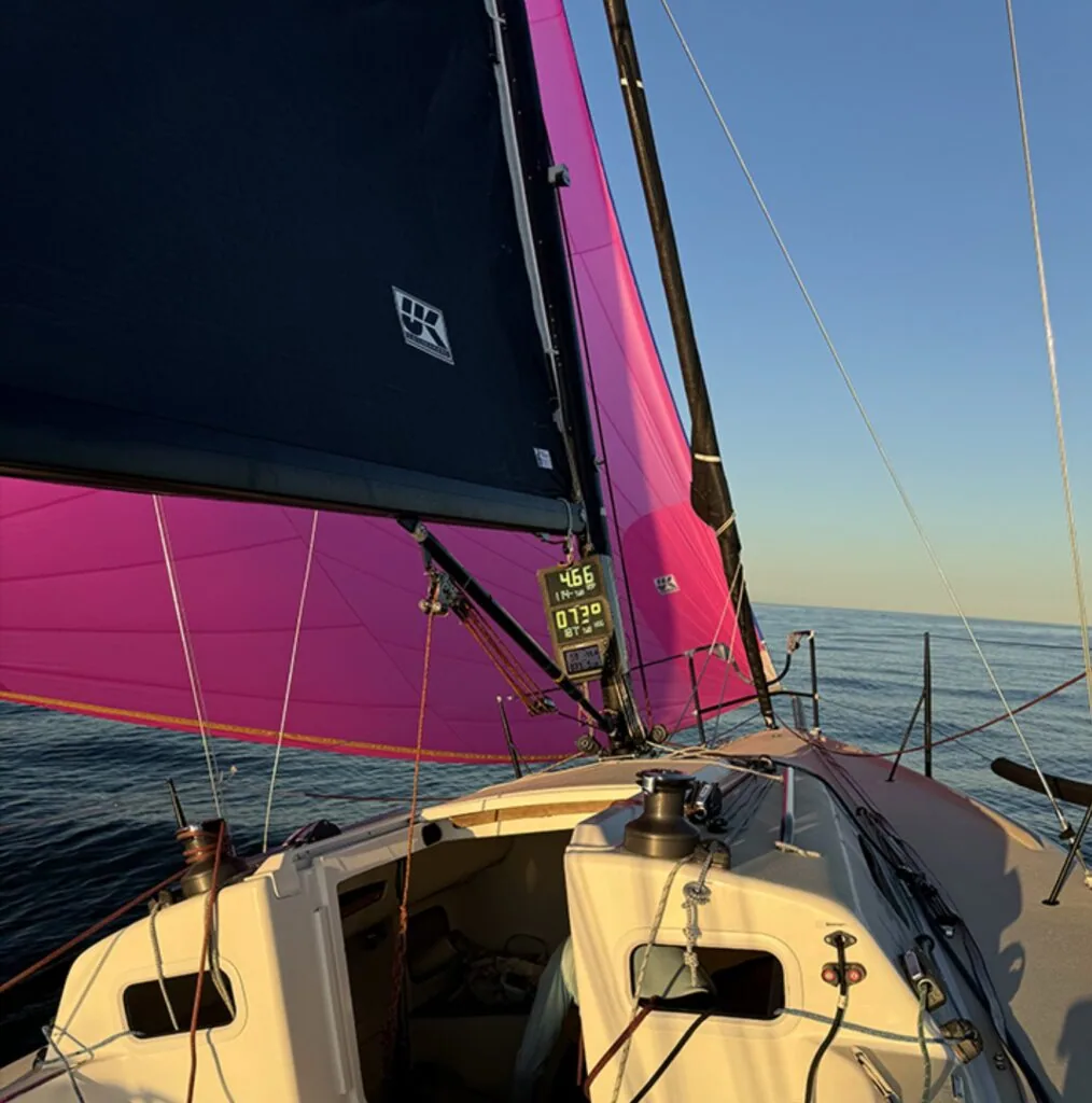 Onboard view looking up at J/88 ONE TOO MANY's magenta spinnaker and mainsail at sunset.