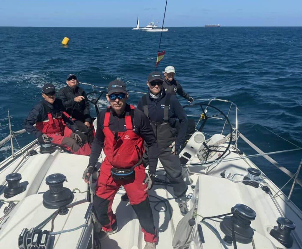 OBSESSION's crew poses on the bow before the start, with a tanker and support boat behind.