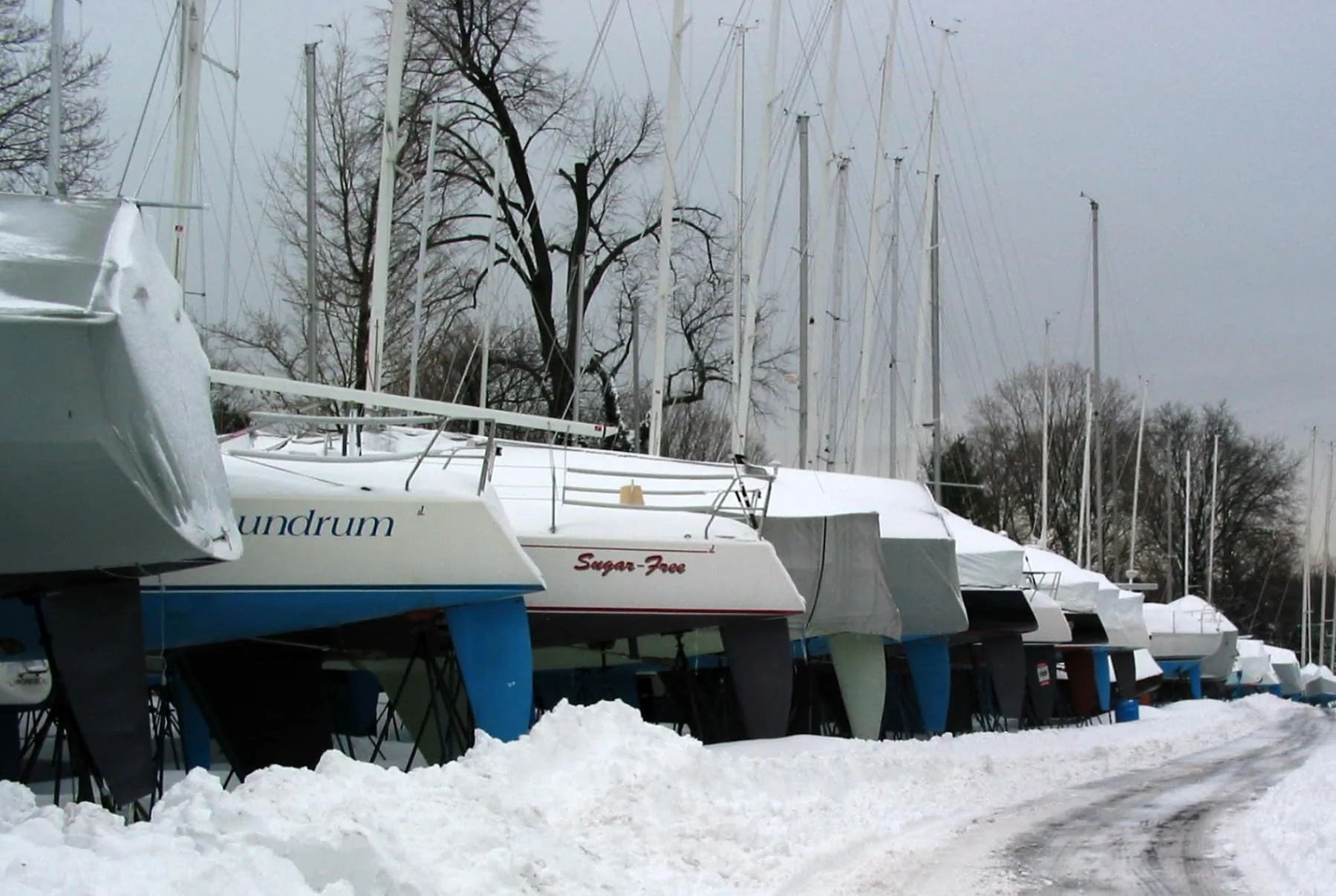 Sailboats shrink-wrapped on stands in a snowy boatyard for winter storage